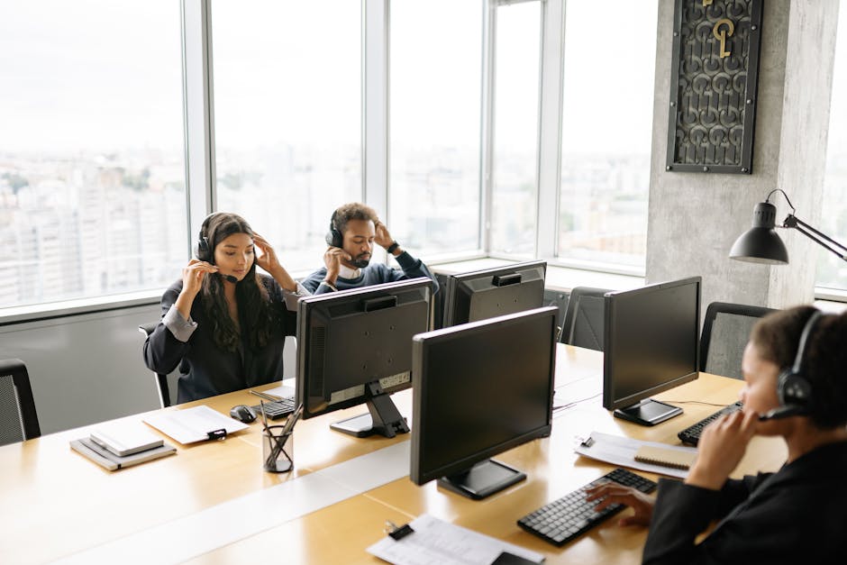 Focused call center agents working at computers with headsets in a bright office setting.